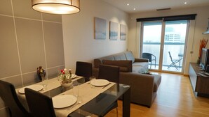 A modern dining area with a glass table, black chairs, and a hanging light fixture. - Apartment in front of Fira Gran Via (Hospitalet de Llobregat - Barcelona)
