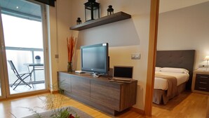 A modern bedroom with a bed, bedside table, and a TV on a wooden cabinet. - Apartment in front of Fira Gran Via (Hospitalet de Llobregat - Barcelona)