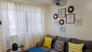 A living room with a grey sofa, a small table with a lamp, decorative pillows, and wall art. - ENTIRE HOUSE/ FULLY AIR CONDITIONED/ HiSpeed Wifi. Cable TV. Smart TV (Pampanga)