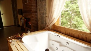 Una bañera de madera con vistas a un bosque a través de una ventana con cortinas translúcidas.