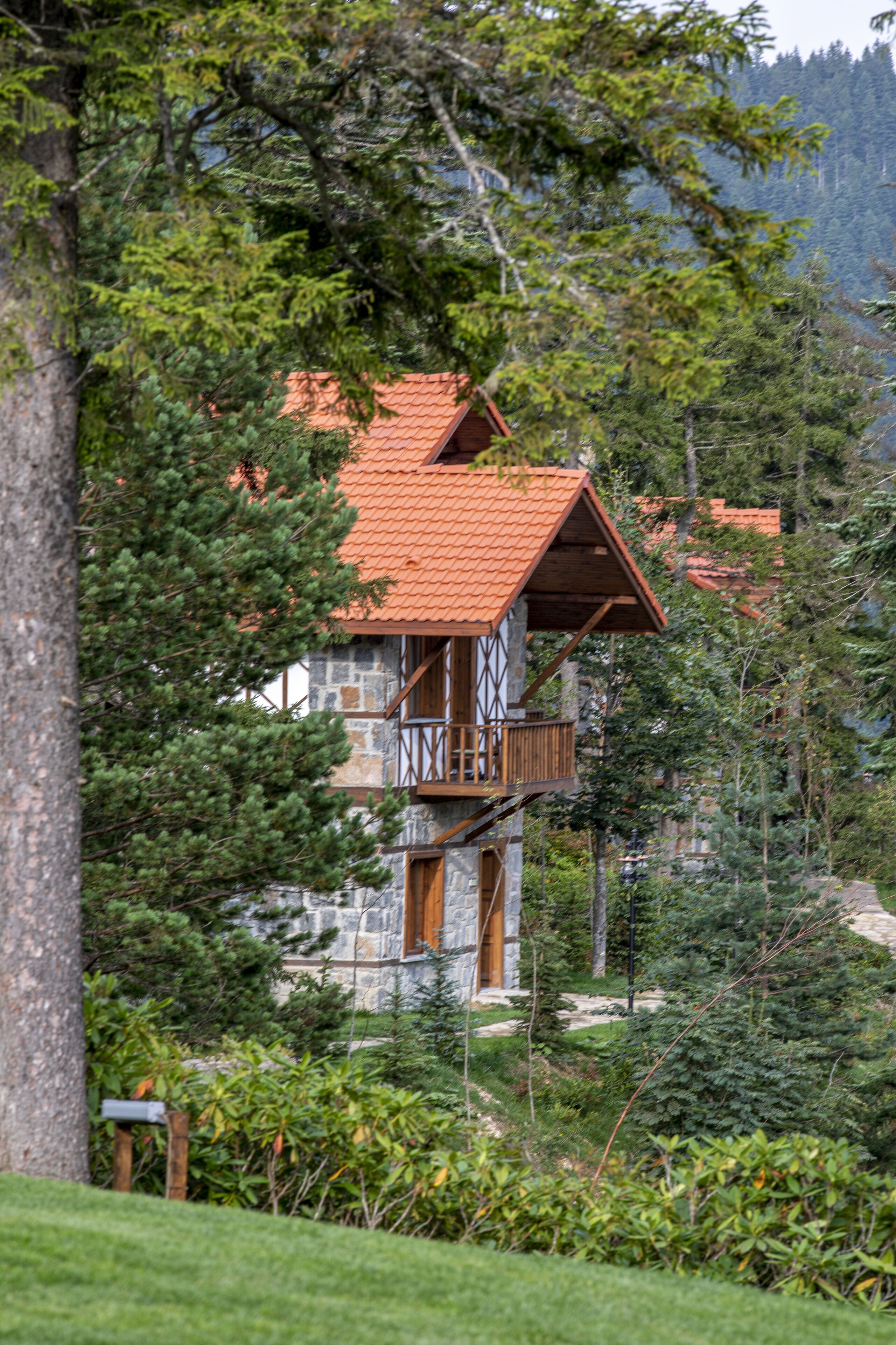 A stone building with a red-tiled roof, a wooden balcony, and surrounded by dense greenery.