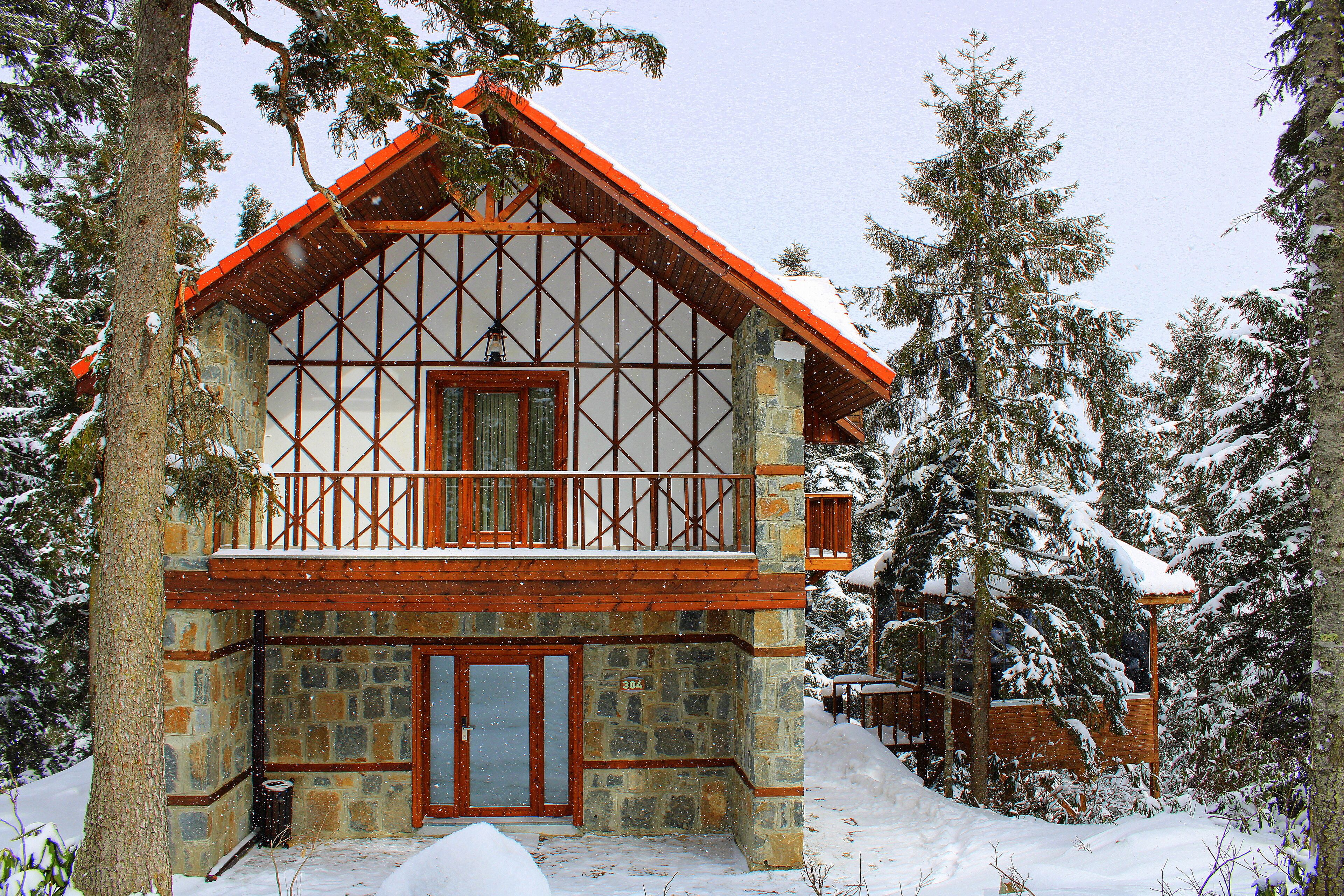 Ein Steinhaus mit einem hölzernen Balkon und einem roten Dach, umgeben von schneebedeckten Bäumen.