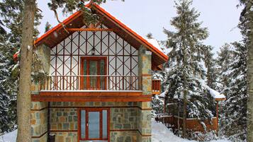 Ein Steinhaus mit einem hölzernen Balkon und einem roten Dach, umgeben von schneebedeckten Bäumen.