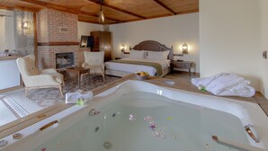 Habitación de hotel con una bañera grande, chimenea, cama con cabecera de madera, una silla y una mesita.