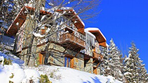 Una cabaña de madera con varios balcones y fachada de piedra, rodeada de árboles cubiertos de nieve.