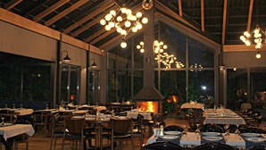 Un comedor interior con mesas dispuestas para una comida, una chimenea grande y abiertos, y lámparas colgantes.