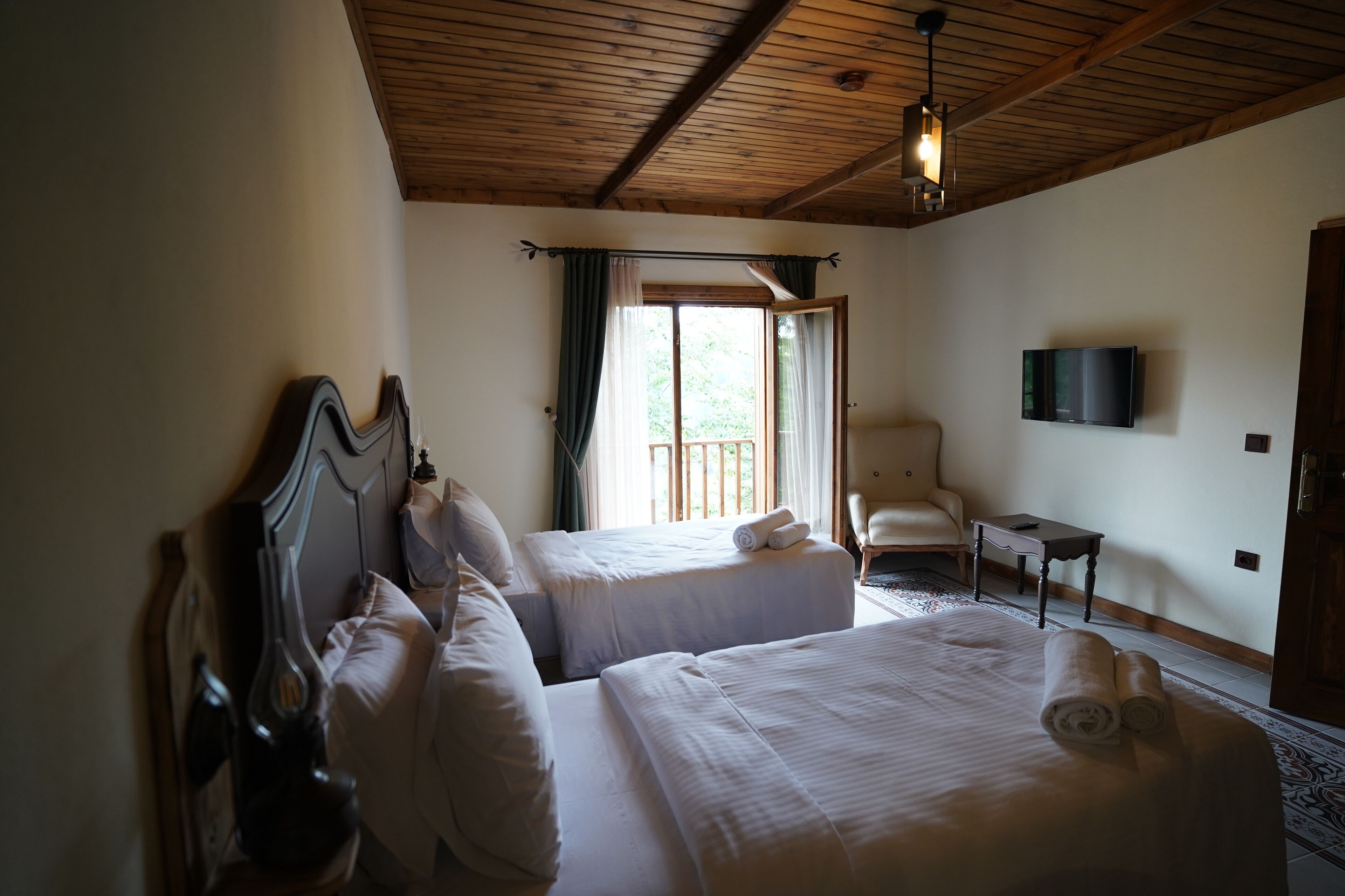 A hotel room with two beds, a TV, a chair, and a balcony with curtains.
