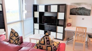 En moderne stue med en rød sofa, mønstrede puder, et sort-hvidt tv-møbel og et billede af bjerge.