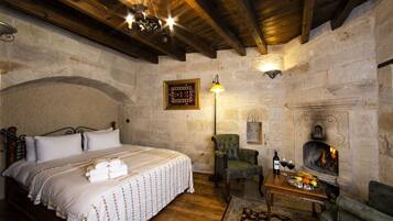 A bedroom with a large bed, a fireplace, a green armchair, and a table with a fruit tray.