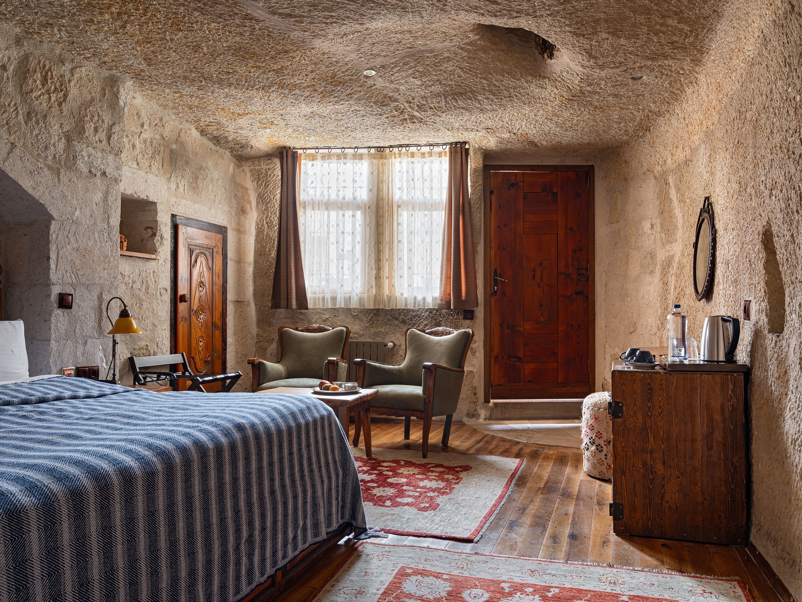 Une pièce rustique comprenant un lit, deux fauteuils, une armoire en bois et une fenêtre avec des rideaux.