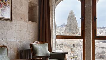 A room with stone walls, two wooden chairs, a table with a metal frame, and a view of rocky terrain through large windows.
