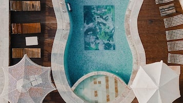 Vista aérea de una piscina con cubierta de madera, sillones de descanso, sombrillas y un borde de mosaicos.