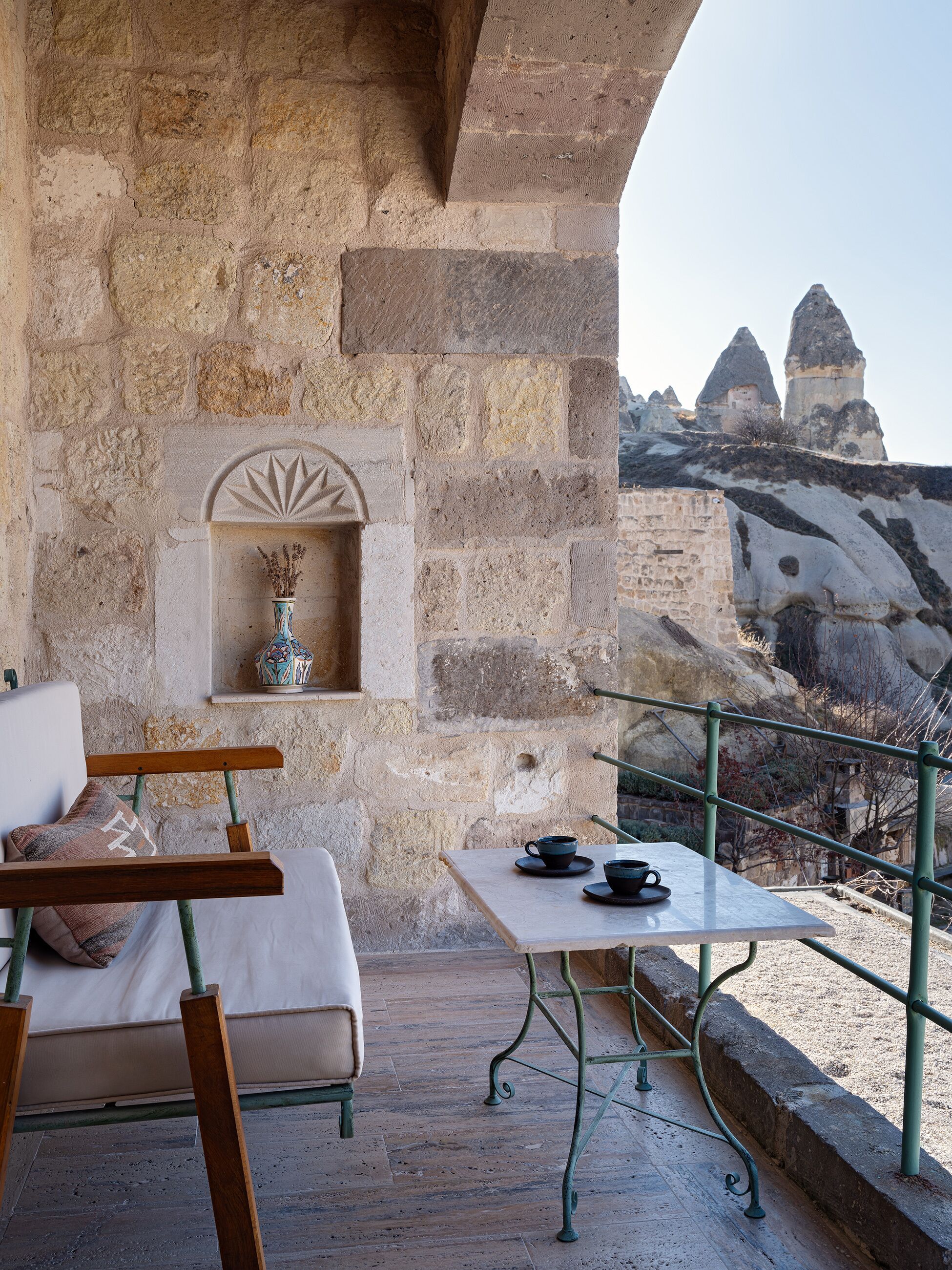 A stone balcony with a table and chairs, a decorative shelf, and a view of rock formations in the distance.