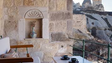 A stone balcony with a table and chairs, a decorative shelf, and a view of rock formations in the distance.