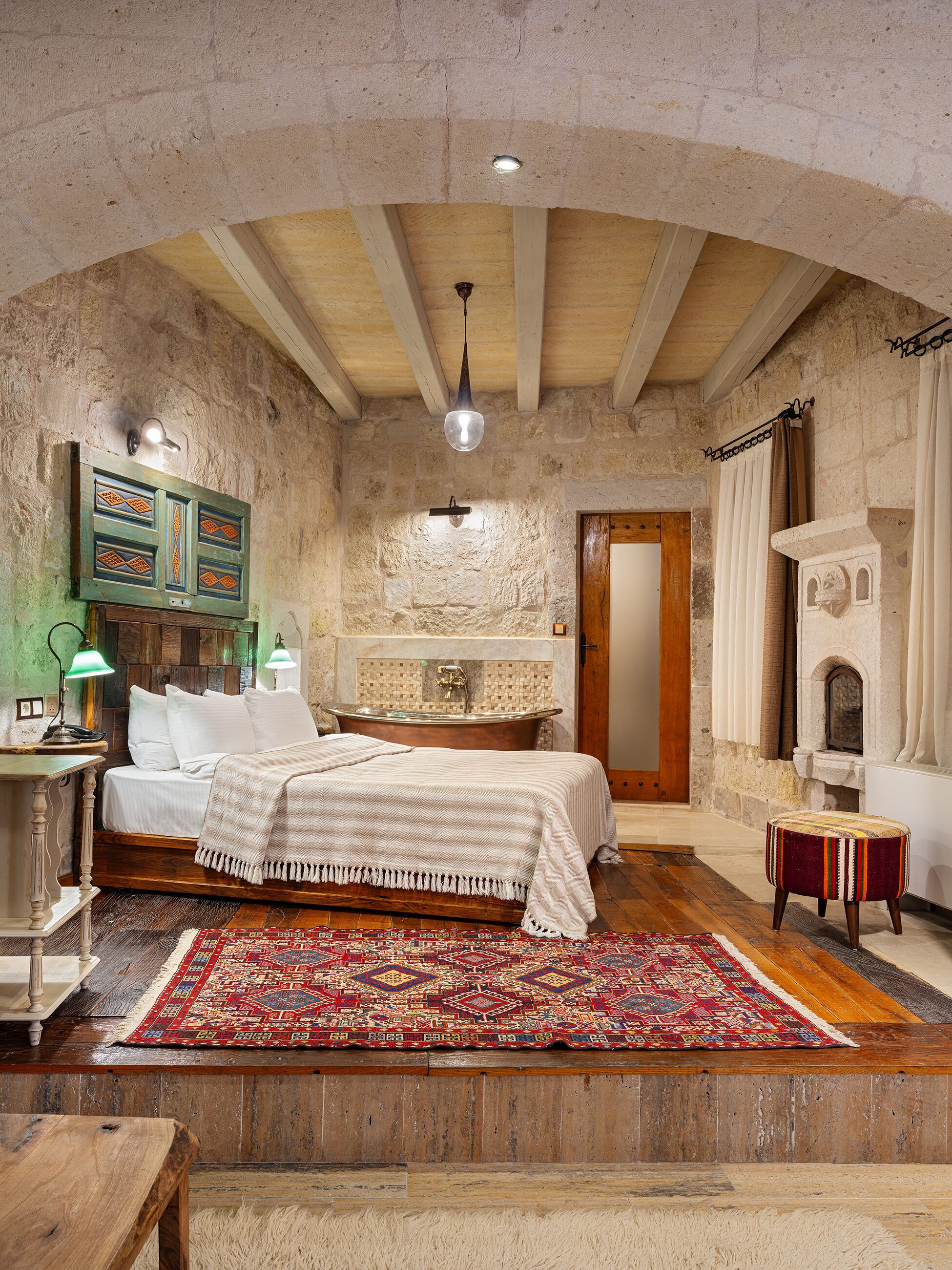 A rustic bedroom with a wooden bed, a large rug, a stone wall, and a fireplace.