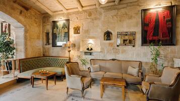 A cozy room with a green sofa, wooden coffee table, and two armchairs. There is a stone wall with a framed tapestry and a mirror.