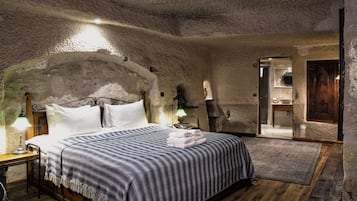 Un dormitorio rústico con una pared de piedra, una cama con manta a rayas y suelo de madera.