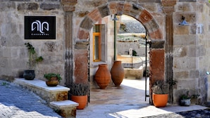 Entrada de um hotel com arco de pedra, plantas em vasos e uma placa indicando o nome do hotel.