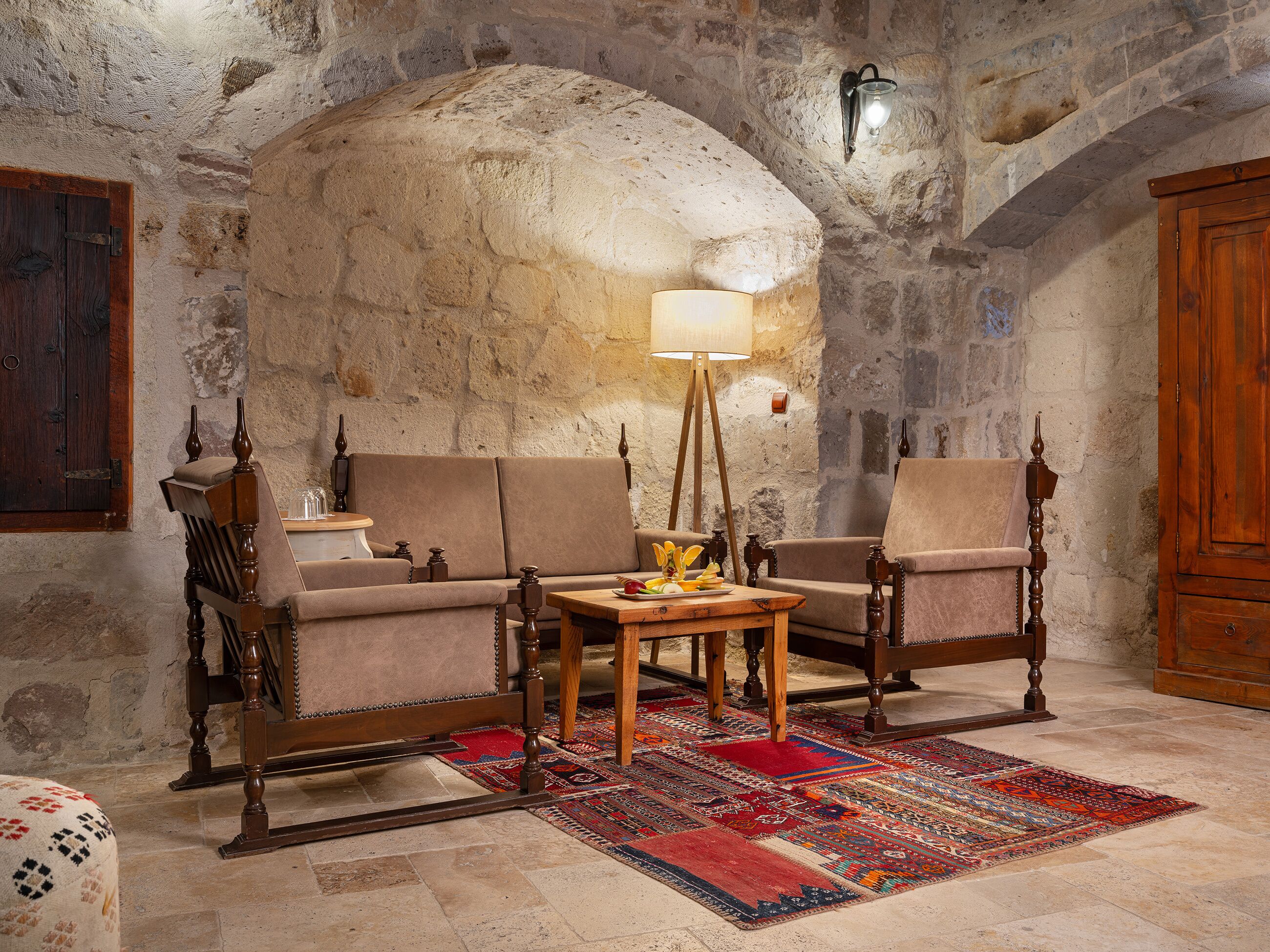 A cozy room with a stone wall, a wooden sofa set, a wooden coffee table, and a patterned rug.