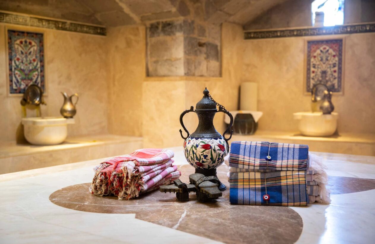 A room with a tiled floor, a decorative metal pitcher, a woven basket, and a folded plaid blanket.