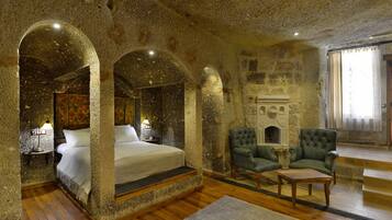 A room with a stone wall bed, two armchairs, a fireplace, and a window with curtains.