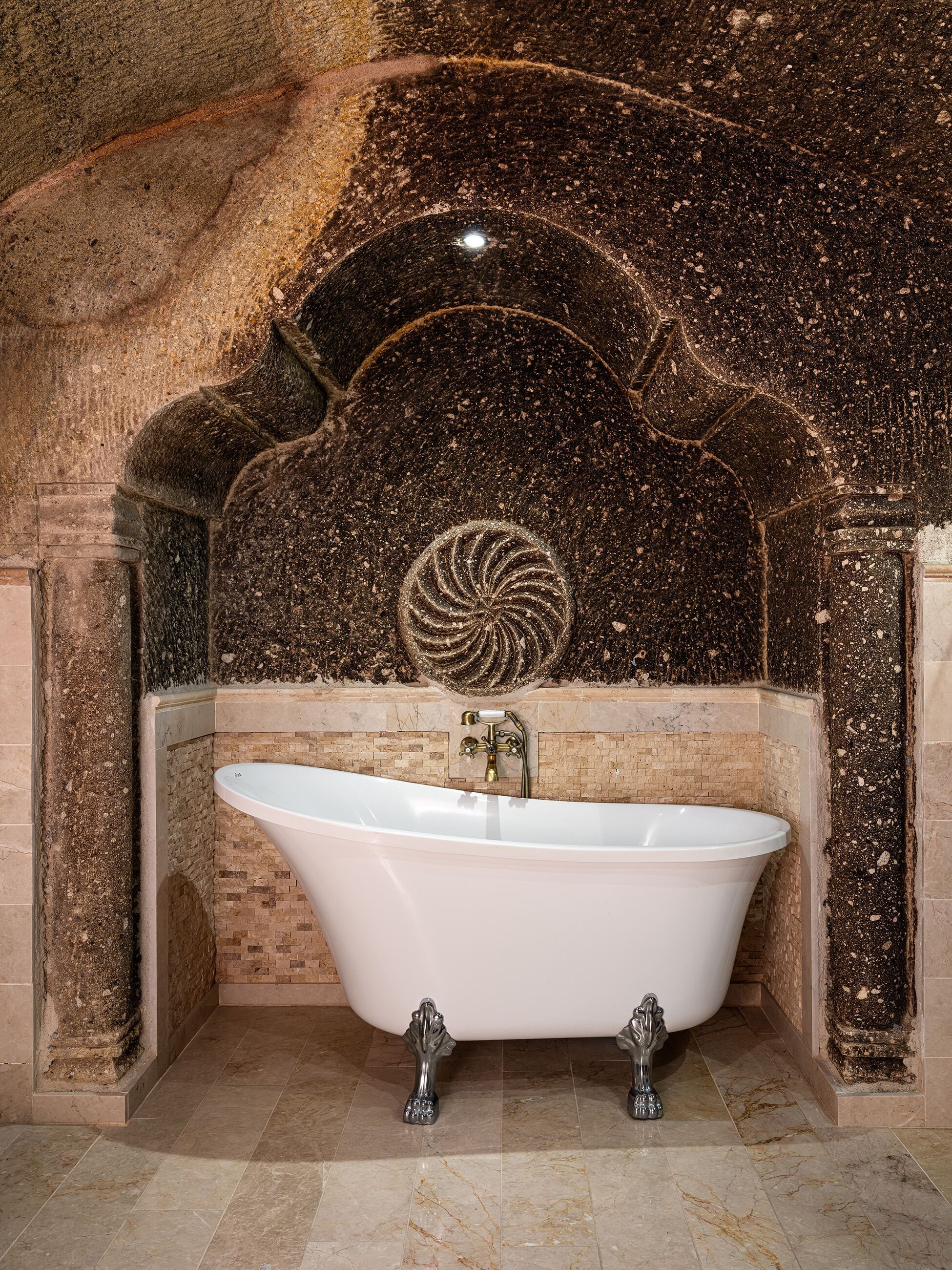 A freestanding bathtub in a stone-walled bathroom with a mosaic design above it.