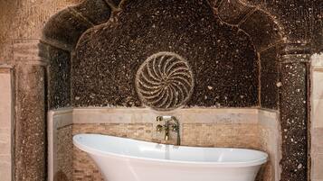 A freestanding bathtub in a stone-walled bathroom with a mosaic design above it.