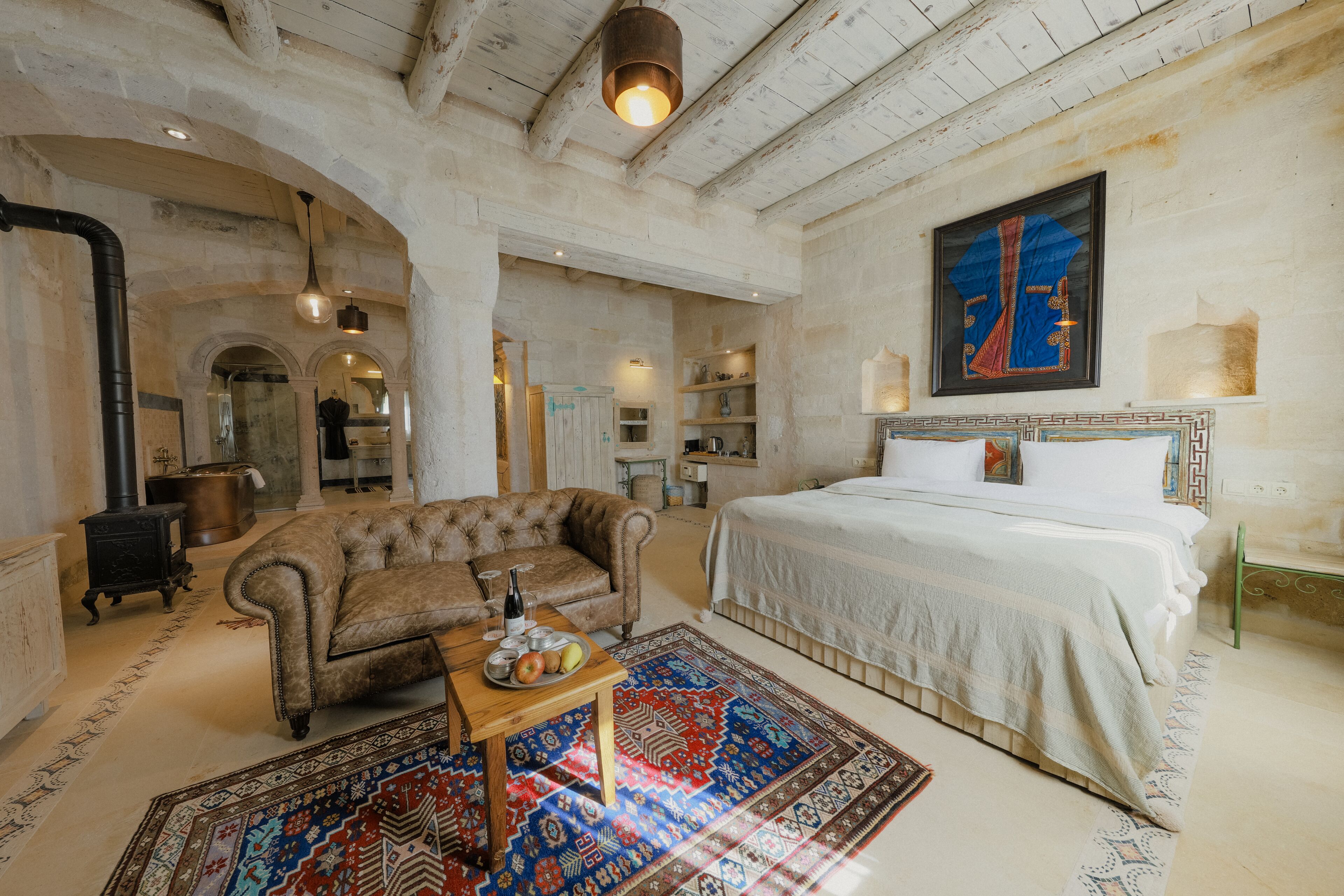 A spacious bedroom with a large bed, a sofa, and a dining table with fruits and a bottle.