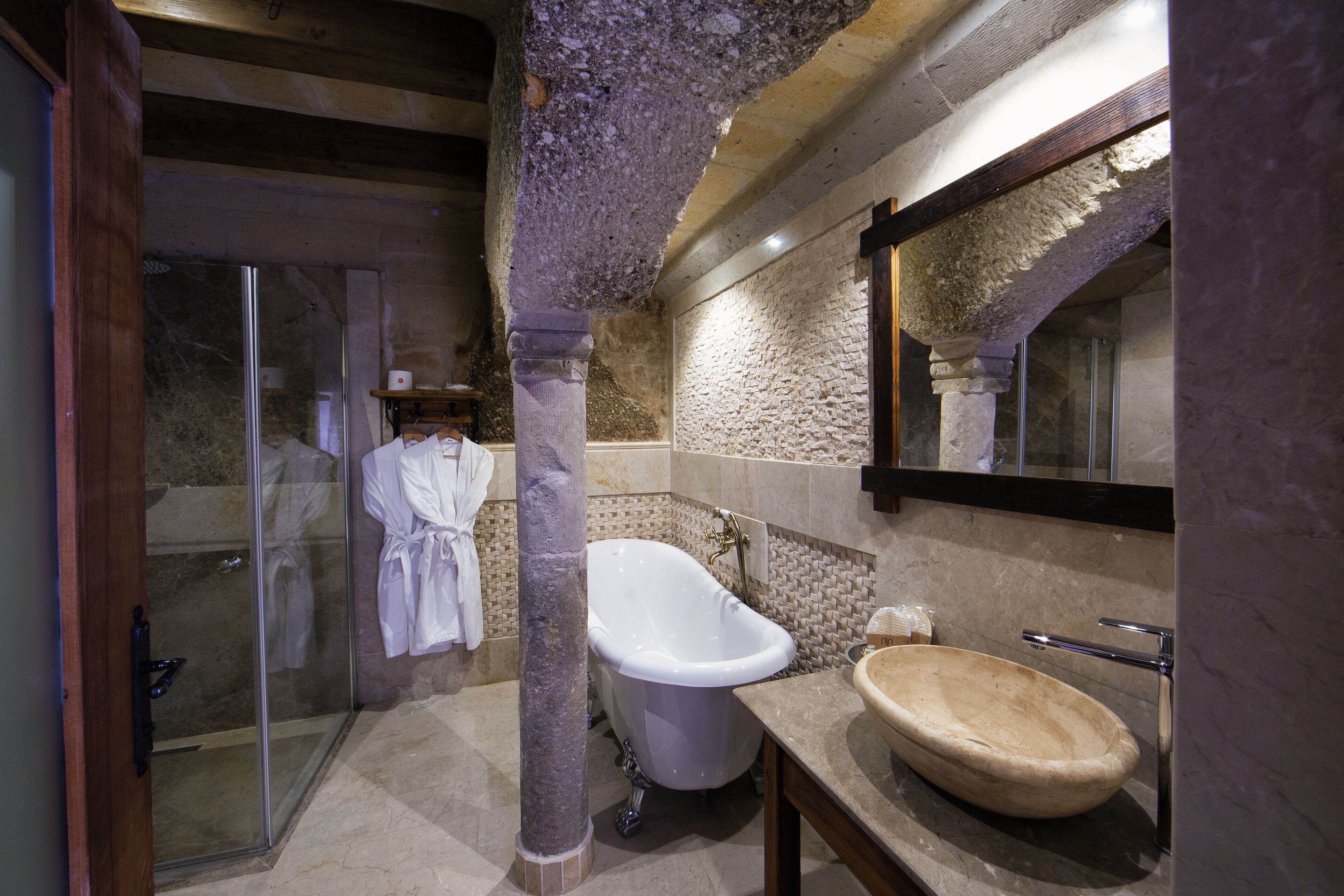 A bathroom with a freestanding bathtub, a glass shower enclosure, and a stone wall.