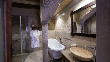 A bathroom with a freestanding bathtub, a glass shower enclosure, and a stone wall.