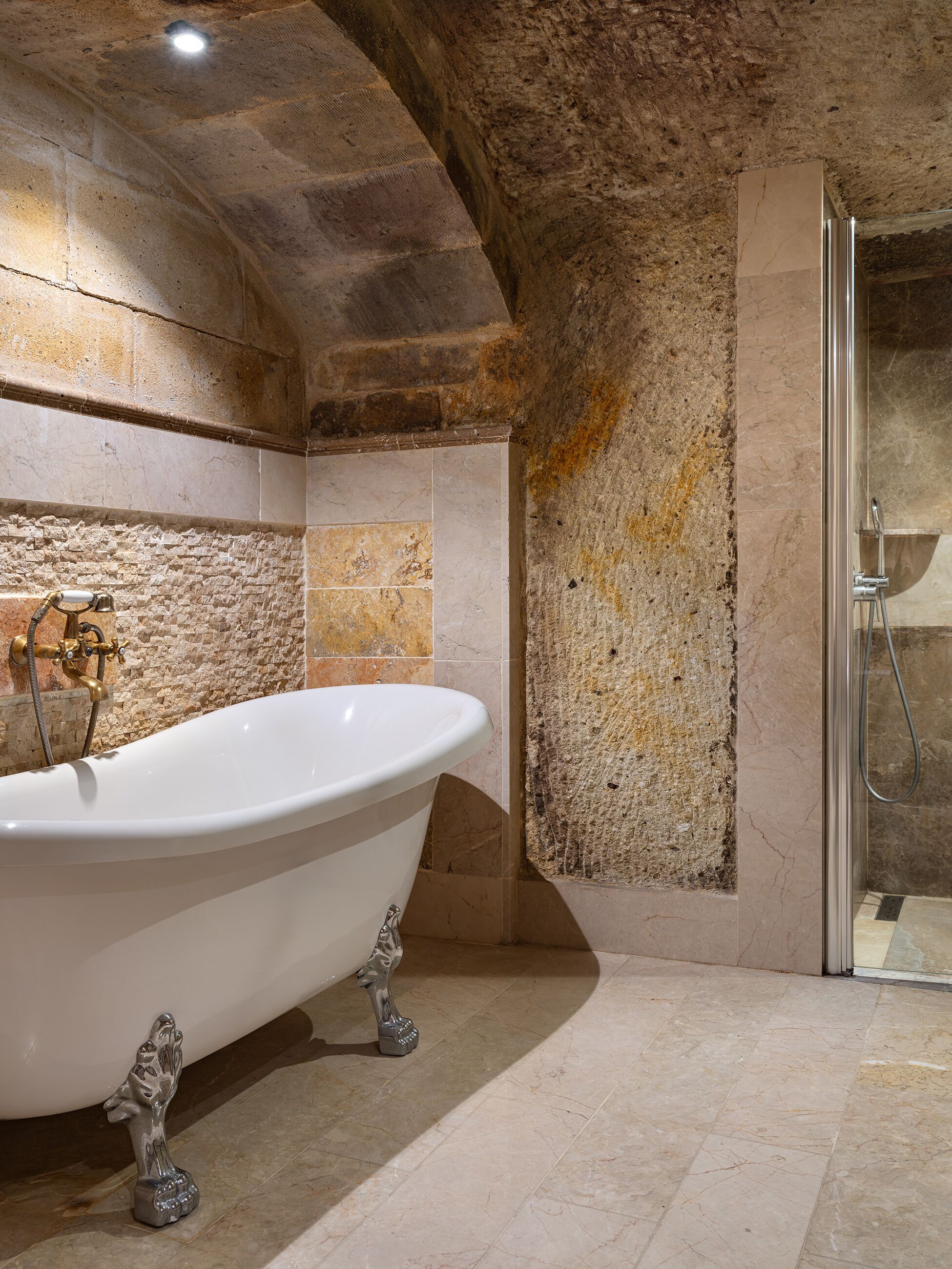Ein Badezimmer mit freistehender Badewanne, einer Dusche und Steinwänden.