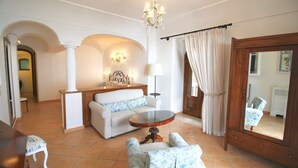 Een ruime woonkamer met een bank, fauteuils, een ronde salontafel, een kroonluchter en een grote spiegel.