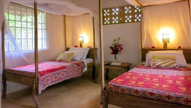 Dos camas individuales con dosel, cabeceros de madera, mesitas de noche con lámparas y un panel decorativo en la pared.