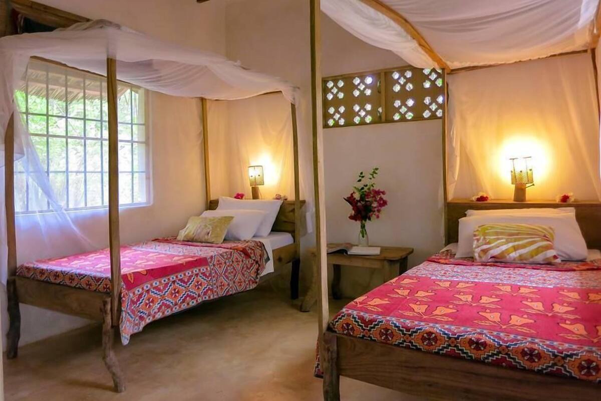 Two single beds with canopy beds, wooden headboards, bedside tables with lamps, and a decorative wall panel.