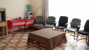 Una habitación con una mesa a cuadros, cinco sillas, un dispensador de agua y un televisor sobre un mueble.