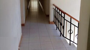 Un pasillo largo y estrecho con pisos de baldosas y una barandilla de madera a la derecha.