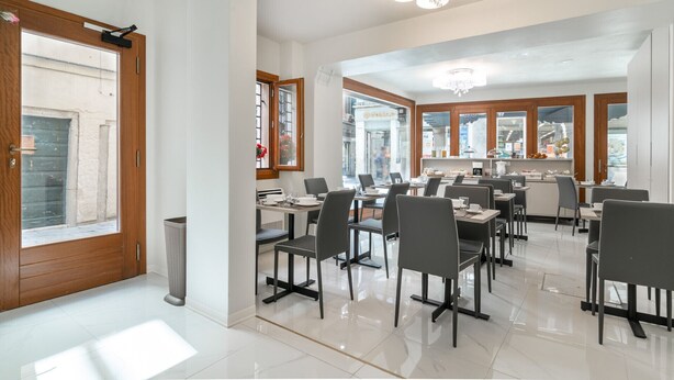 Een moderne eetruimte met meerdere tafels en stoelen, een kroonluchter en grote ramen met uitzicht op de straat.