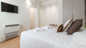 Een moderne slaapkamer met een bed, witte lakens, een flatscreen-tv en een wandairconditioner.