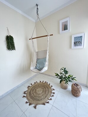 Une pièce avec un fauteuil suspendu, un tapis tissé et deux plantes en pot.