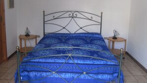 Una cama con colcha azul estampada, dos mesitas de noche con lámparas y un cabecero de metal.