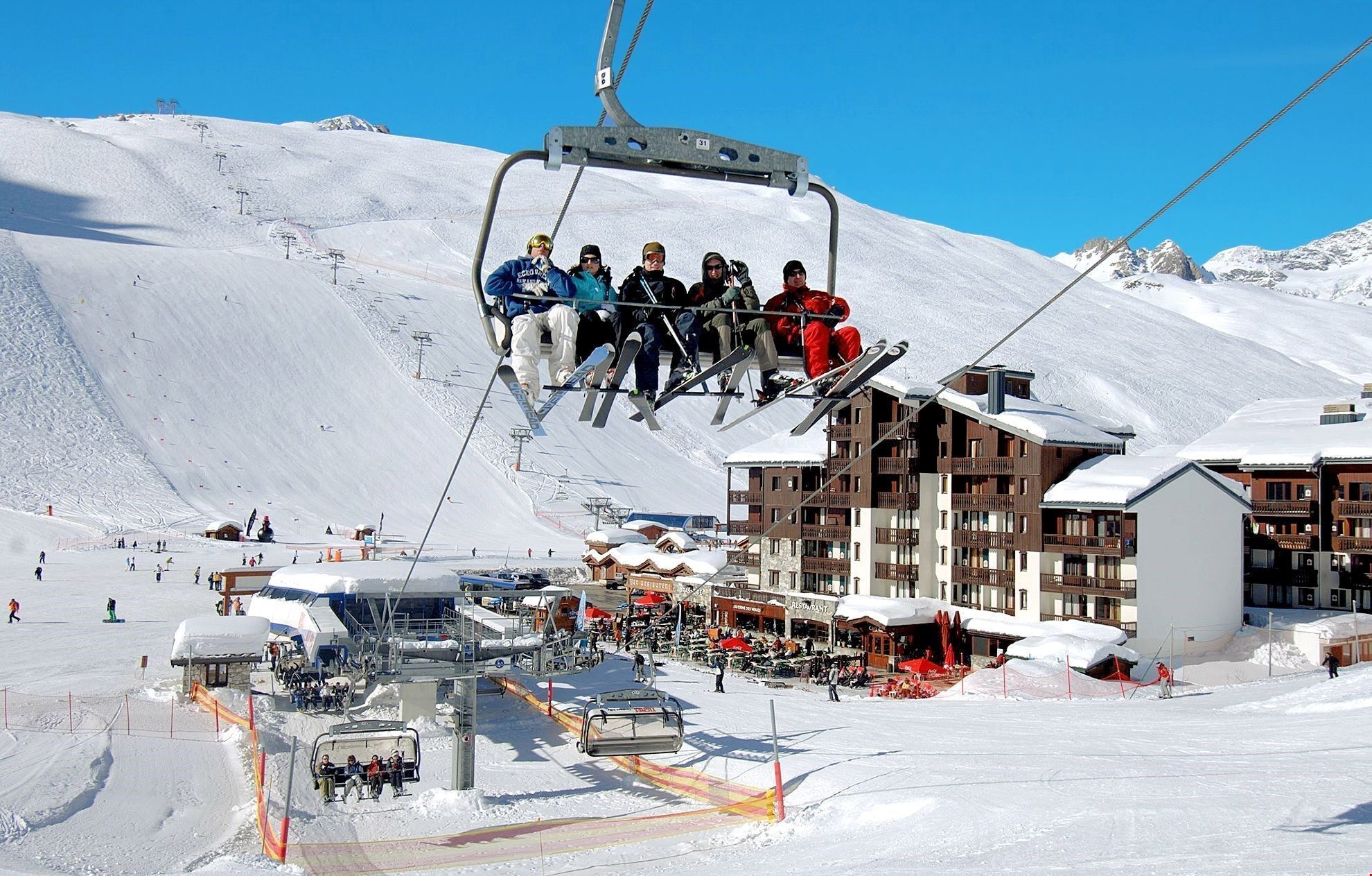 A ski lift with skiers, a ski resort with buildings, and a snowy landscape.