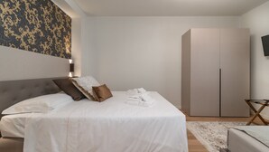 Een moderne slaapkamer met een bed, kussens, een nachtkastje, een stoel, een kledingkast en een televisie.