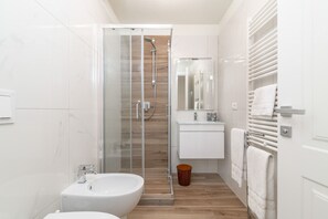 Un baño moderno con cabina de ducha de vidrio, un lavabo blanco y un perchero para toallas.
