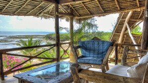 A wooden outdoor seating area with a glass table, a blue patterned chair, and a view of the beach and ocean. - VILLA FUKU - Four Bedroom Villa, Sleeps 10 (Zanzibar)