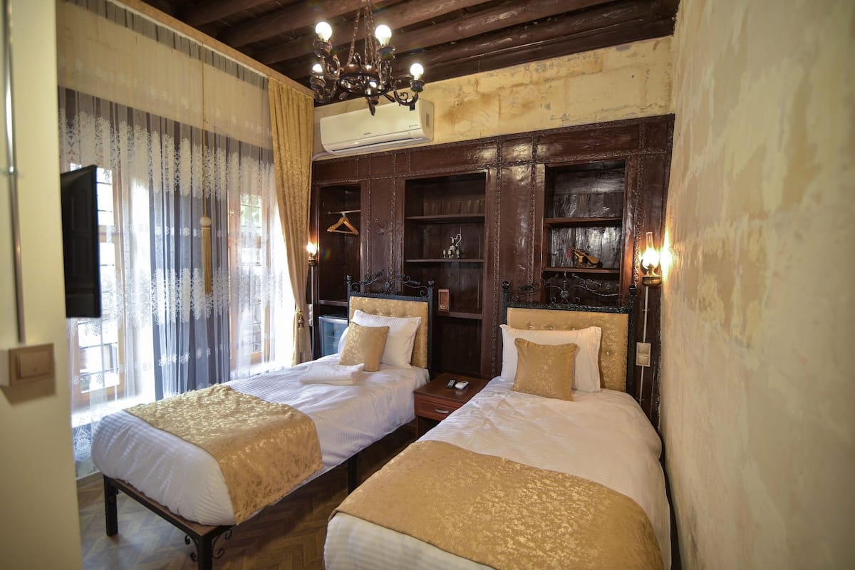 A room with two beds, a chandelier, an air conditioning unit, and a wooden headboard.