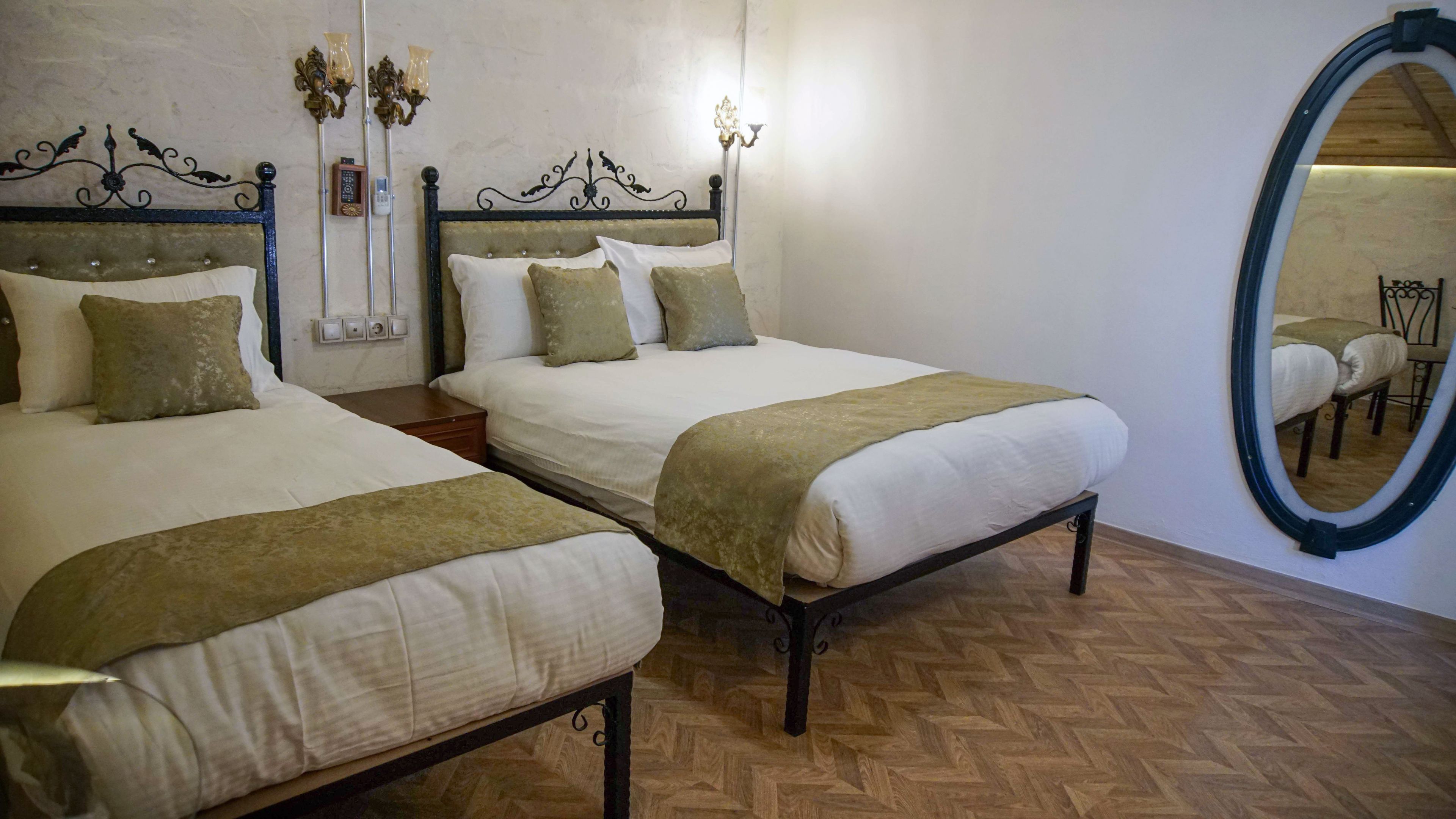 A hotel room with two beds, a mirror, and a wall-mounted light fixture.