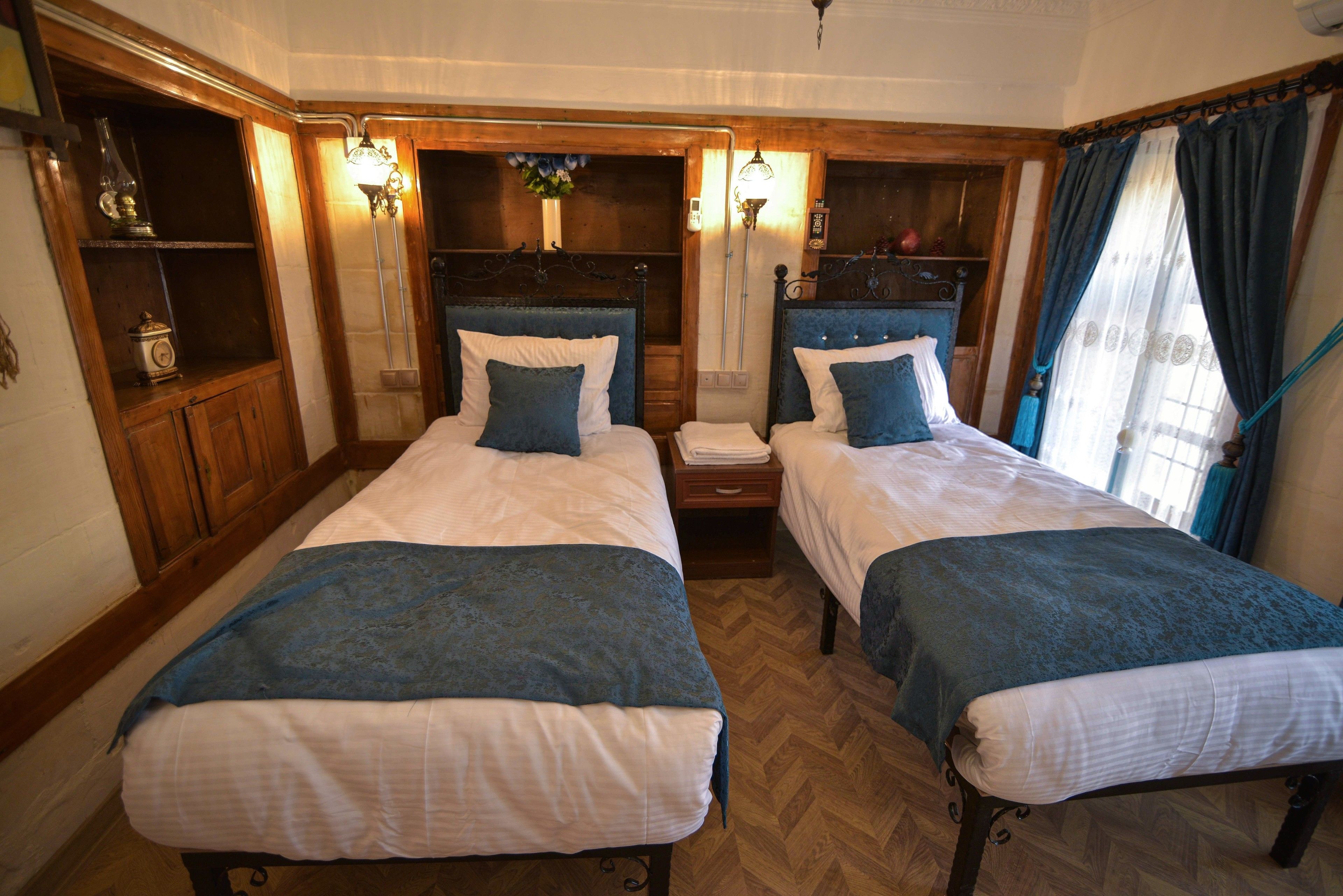 A room with two beds, wooden headboards, and a herringbone floor pattern.