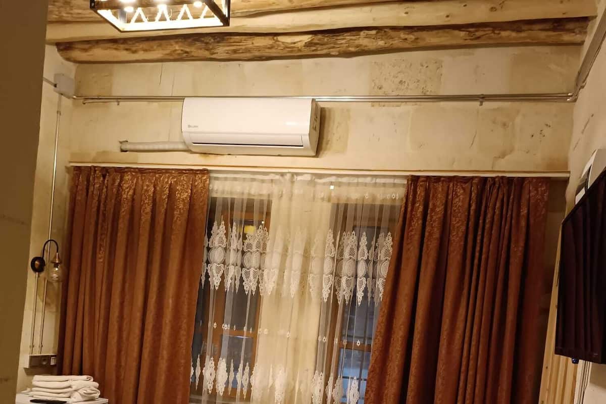 A room with a bed, a window with curtains, an air conditioning unit, and a wooden ceiling.