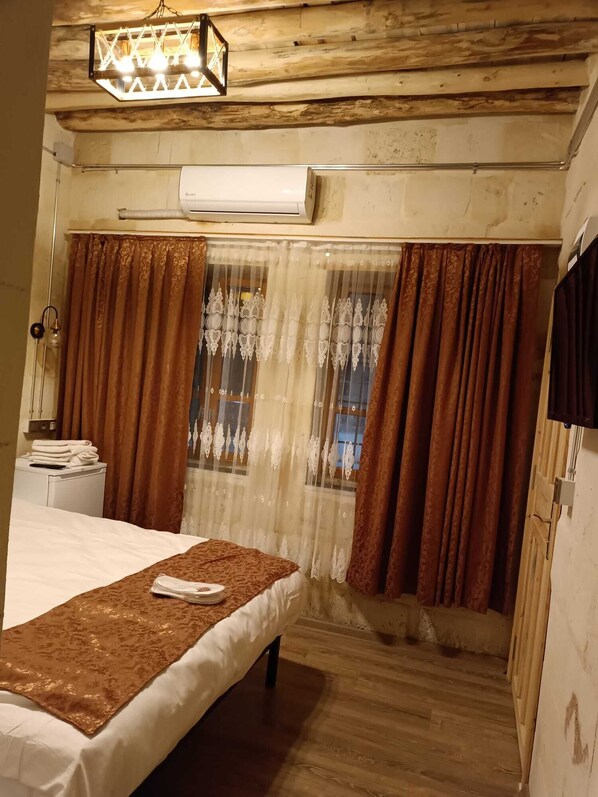 A room with a bed, a window with curtains, an air conditioning unit, and a wooden ceiling. - DOĞANBEY KONAĞI (Gaziantep)