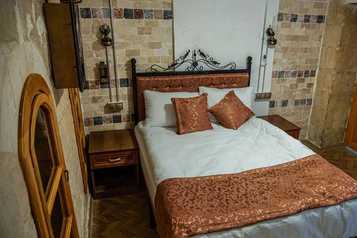 A neatly made bed with a white and copper-colored bedspread, two matching pillows, and a wooden headboard.